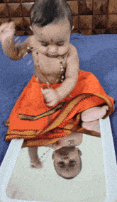 a baby is sitting on a bed and looking at his reflection in a mirror