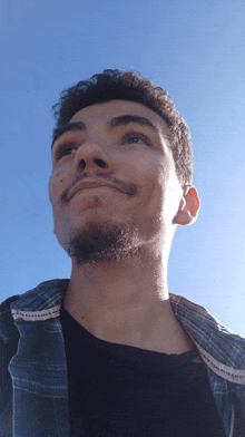 a man wearing a plaid shirt and a black shirt looks up at the sky