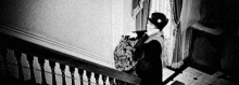a black and white photo of a woman standing on a set of stairs holding a bag .