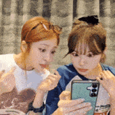 two girls are looking at a cell phone and one of them is wearing a shirt that says twentyfourtwenty