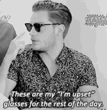 a black and white photo of a man wearing sunglasses and a floral shirt .