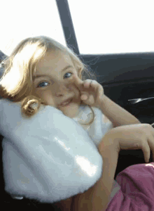 a little girl sitting in a car with a white pillow on her neck