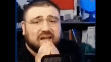 a man with glasses is crying while sitting in front of a microphone in a room .