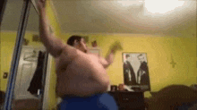 a shirtless man is dancing in a room with a picture of two men on the wall .
