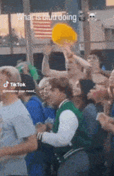 a man in a green jacket is dancing in a crowd of people with the caption what is bud doing