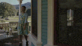a woman in a dress is standing on a porch next to a house .