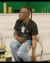 a man with dreadlocks is sitting on a couch wearing a black shirt with the letter k on it