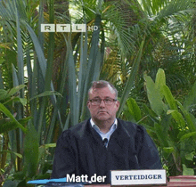 a man in a judge 's robe sits in front of a sign that says matt der verteidiger