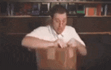 a man in a white shirt is opening a cardboard box in front of a shelf .