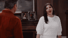 a woman in a white sweater stands in front of a man in a red shirt in a living room