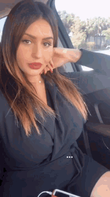 a woman in a black dress is sitting in a car with her hand on her face