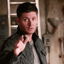 a man in a black jacket is pointing his finger at something .