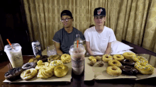 two men sit at a table with donuts and drinks including a can of rockstar