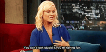 a woman in a blue shirt is sitting on a couch and saying you can 't look stupid if you are having fun