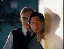 two men are standing next to each other in front of a wall .