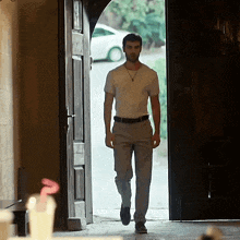 a man in a white shirt and gray pants is walking through an open door