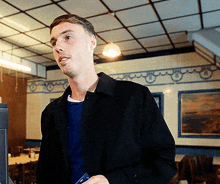 a man in a black jacket is standing in a room with a picture on the wall