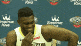 a man in a smoothie king jersey laughs in front of a blue backdrop