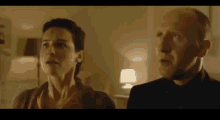 a man and a woman are standing next to each other in a living room looking at something .