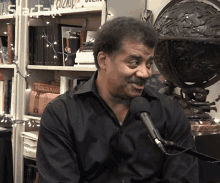 a man in a black shirt is talking into a microphone in front of a shelf with a book called dictionary