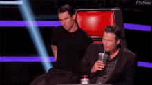 a man in a suit is sitting in a chair next to a man in a plaid shirt .