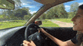 a woman is driving a volkswagen car with a park in the background