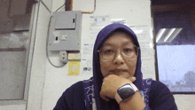 a woman wearing glasses and a purple head scarf has her hand under her chin