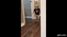 a baby is walking on a wooden floor in a room .