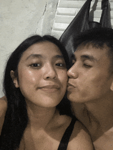 a man kisses a woman on the cheek in front of a white wall