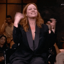 a woman in a black suit is sitting in a chair with her hands in the air