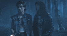 two men are standing in a dark forest and one has a shirt that says club