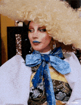a woman wearing a wig and a blue scarf around her neck is looking at the camera .