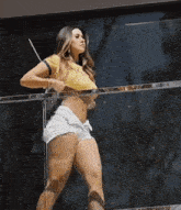 a woman in a yellow crop top and white shorts is standing next to a railing .