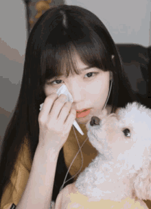 a girl wipes her nose with a napkin while holding a small dog