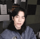 a young man is sitting in a chair in a room wearing a blue jacket and a black hoodie .
