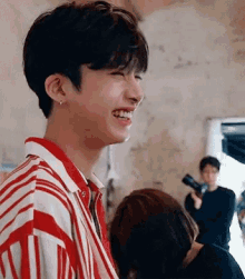a young man wearing a red and white striped shirt is smiling while standing next to a woman .