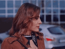 a woman wearing a brown jacket and a scarf is standing in front of a white car .
