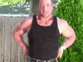 a man wearing a black tank top is standing in front of a wooden fence