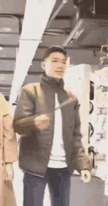 a man in a brown jacket is standing in a store holding a sword .