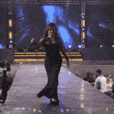 a woman in a black dress is walking down a stage