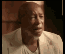 a bald man with a beard is crying while wearing a white suit and a white shirt .