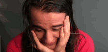 a man with long hair is covering his face with his hands while crying .