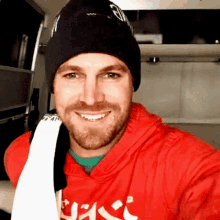 a man wearing a red hoodie and a black beanie smiles