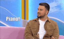 a man with a beard is sitting on a pink couch with the words piano written on the screen behind him