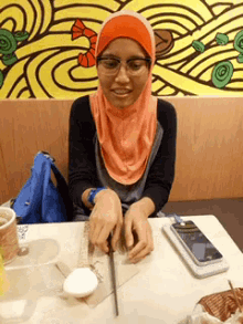 a woman in a hijab sits at a table with a cell phone and a cup of tea