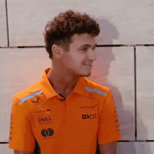 a man in an orange shirt is standing in front of a wall and smiling .