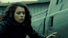 a woman in a black jacket is reaching into a truck door .