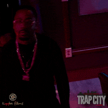 a poster for trap city features a man in a suit and glasses