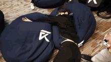 a person is laying on a blue bean bag chair with a white letter k on it