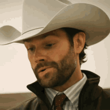 a man with a beard wears a white cowboy hat